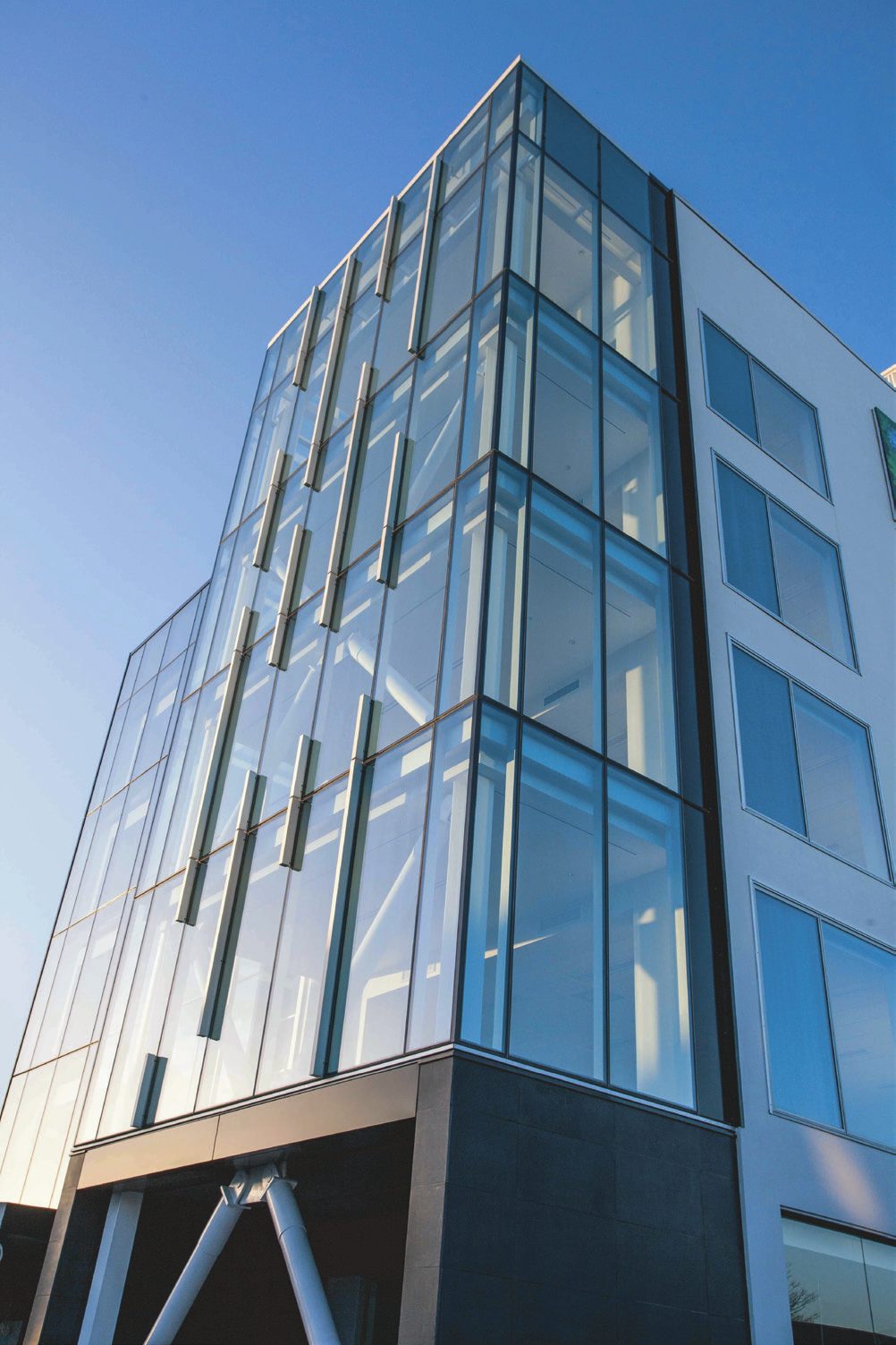 Four-storey glazed curtain wall corner with vertical aluminium fins against a clear sky